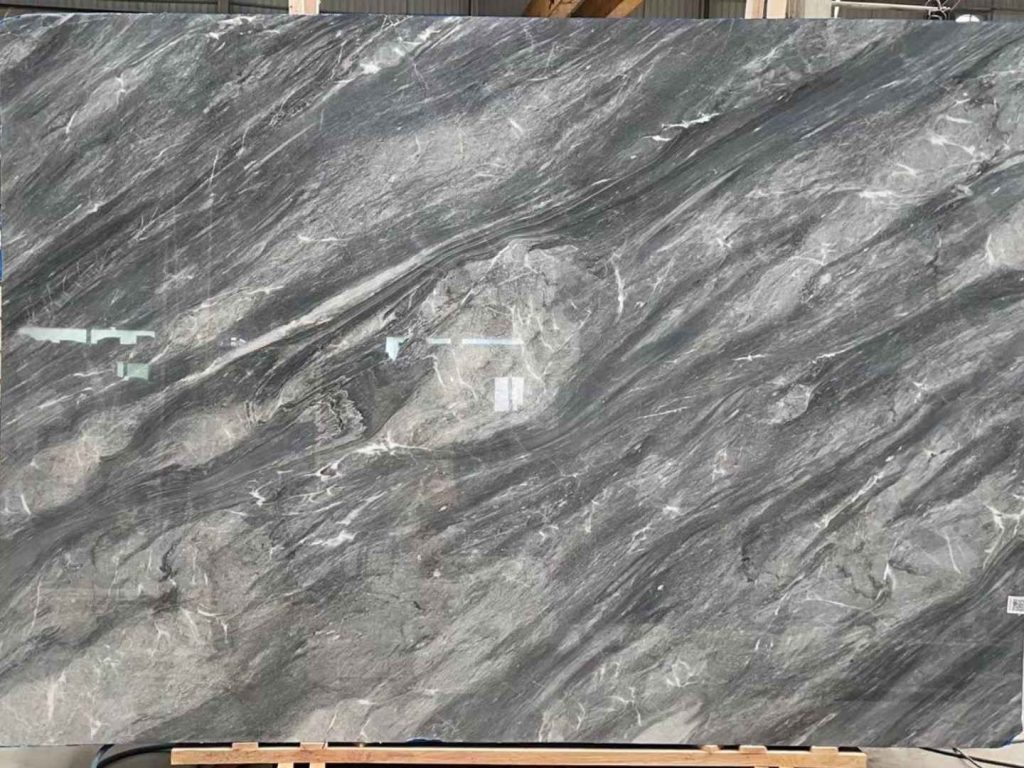 A large slab of polished marble with swirling patterns of dark grey, light grey, and thin white veins.