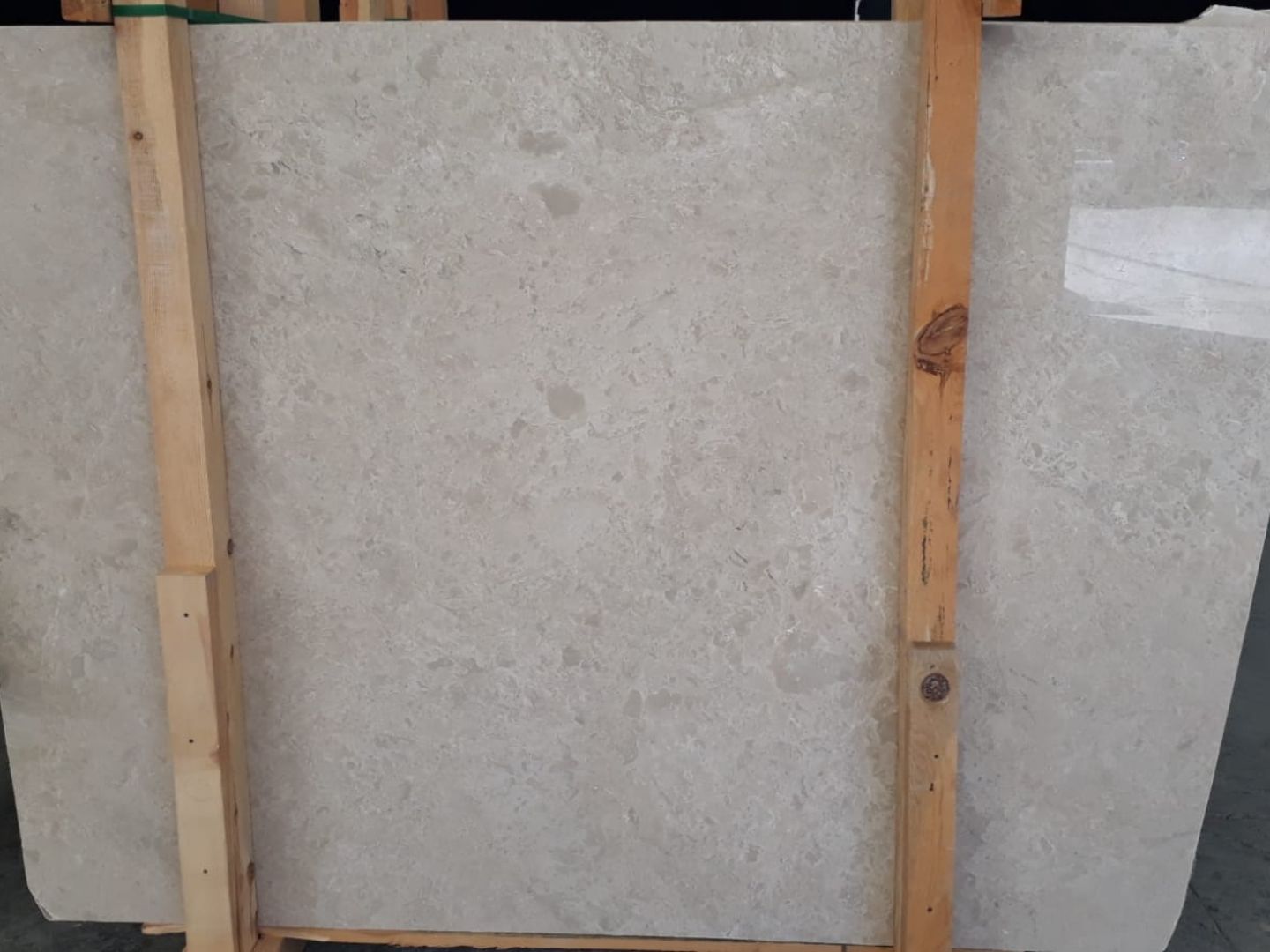 A large, polished slab of light beige stone with subtle variations in tone and small, irregular darker speckles. The surface